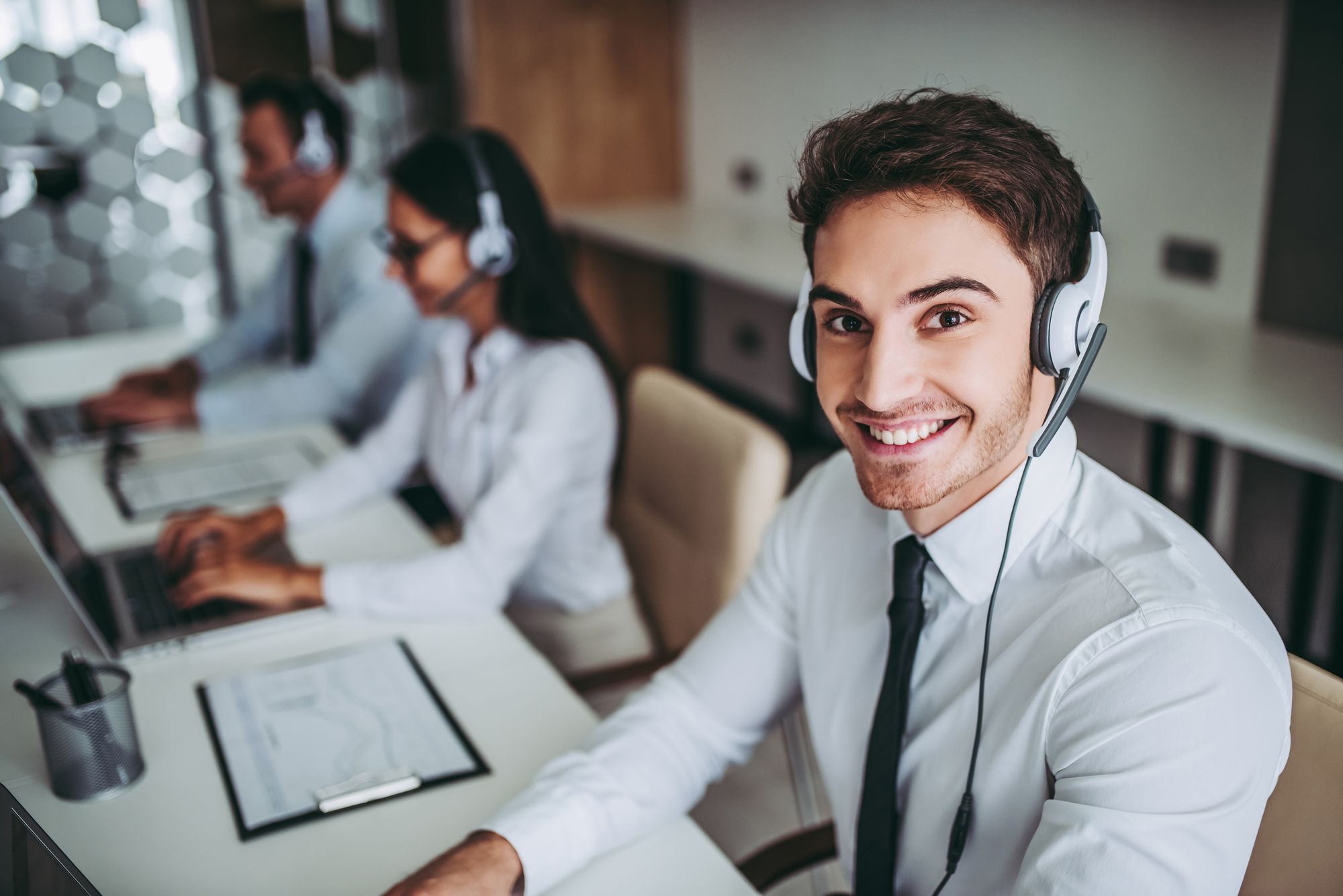 How can I help you? Beautiful call center workers in headphones are working at modern office.